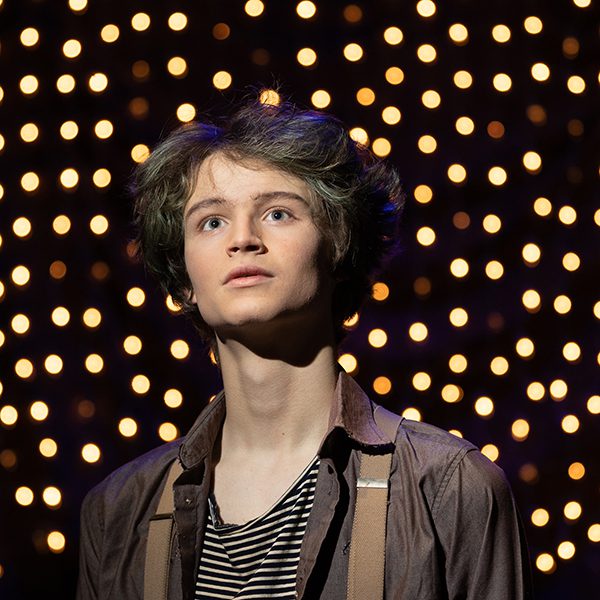 boy staring off into space with twinkle lights behind him